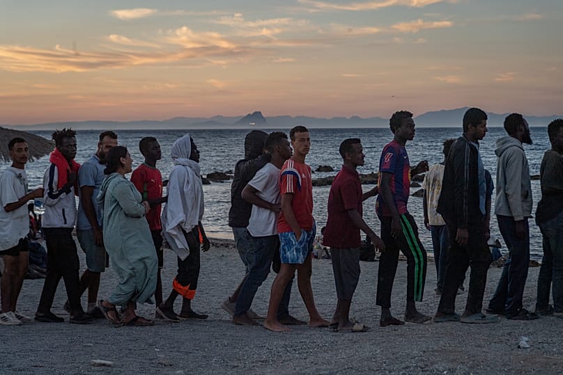 Migrants who crossed from Morocco into Spain line up for food distribution on a beach in the Spanish enclave of Ceuta, 3 August, 2026