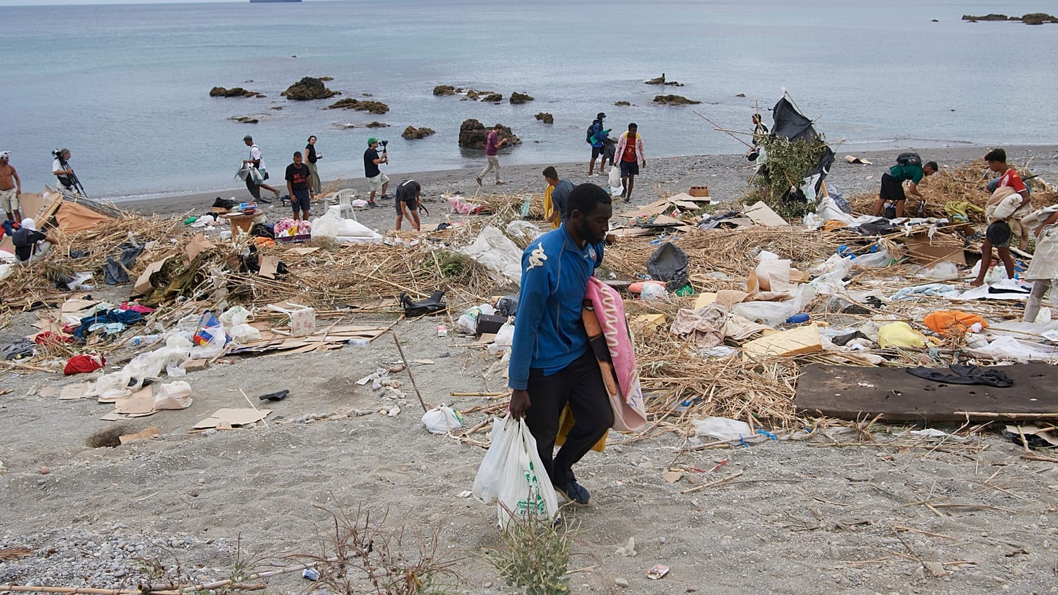 Varios inmigrantes que cruzaron de Marruecos a España recogen sus pertenencias tras ser desalojados de una playa en Ceuta, el jueves 20 de agosto de 2026