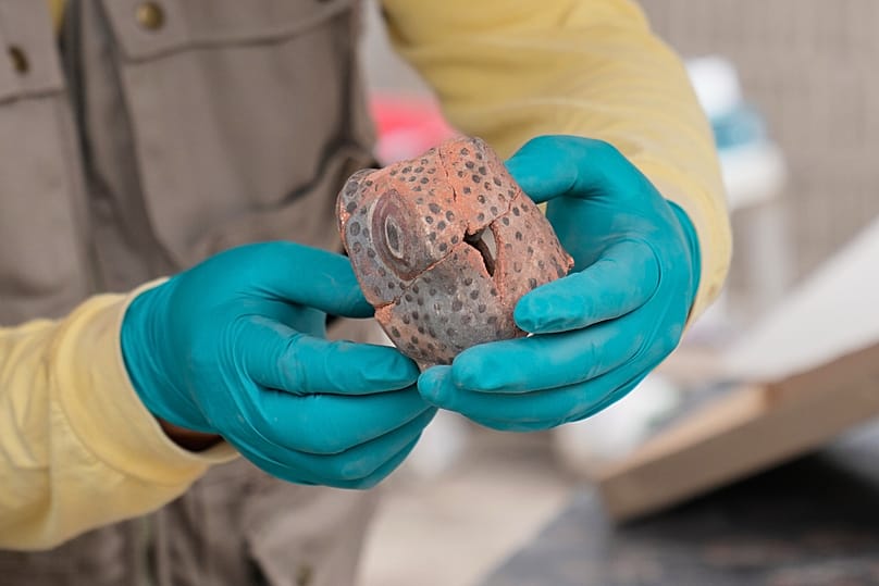 An archaeologist holds up a ceramic snake head that he unearthed while excavating skeletal remains at the Huaca Pucllana archaeological site in Lima, Peru.