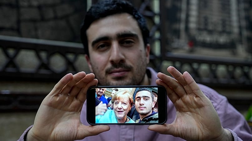  اللاجئ السوري أنس مودماني (27 عاماً) يعرض صورته "السيلفي" الشهيرة مع ميركل داخل مطعم ببرلين، 10 ديسمبر 2024.