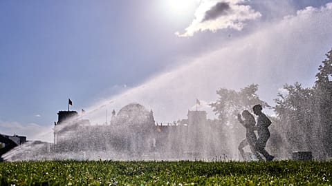 Unas mujeres pasan corriendo junto a un aspersor frente al edificio del Reichstag en una mañana de verano en Berlín, 11 de agosto de 2026