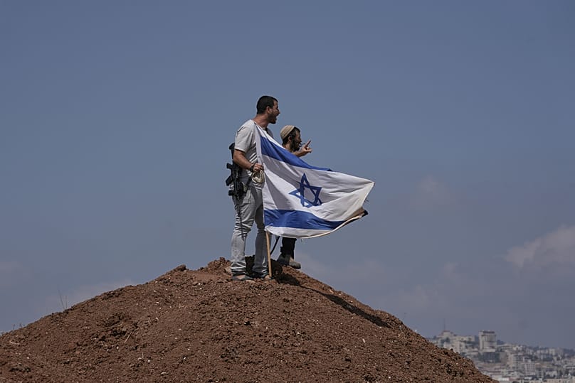 Israeli settlers put up an Israeli flag on a hilltop on the outskirts of the West Bank city of Beit Sahour, 14 August, 2026