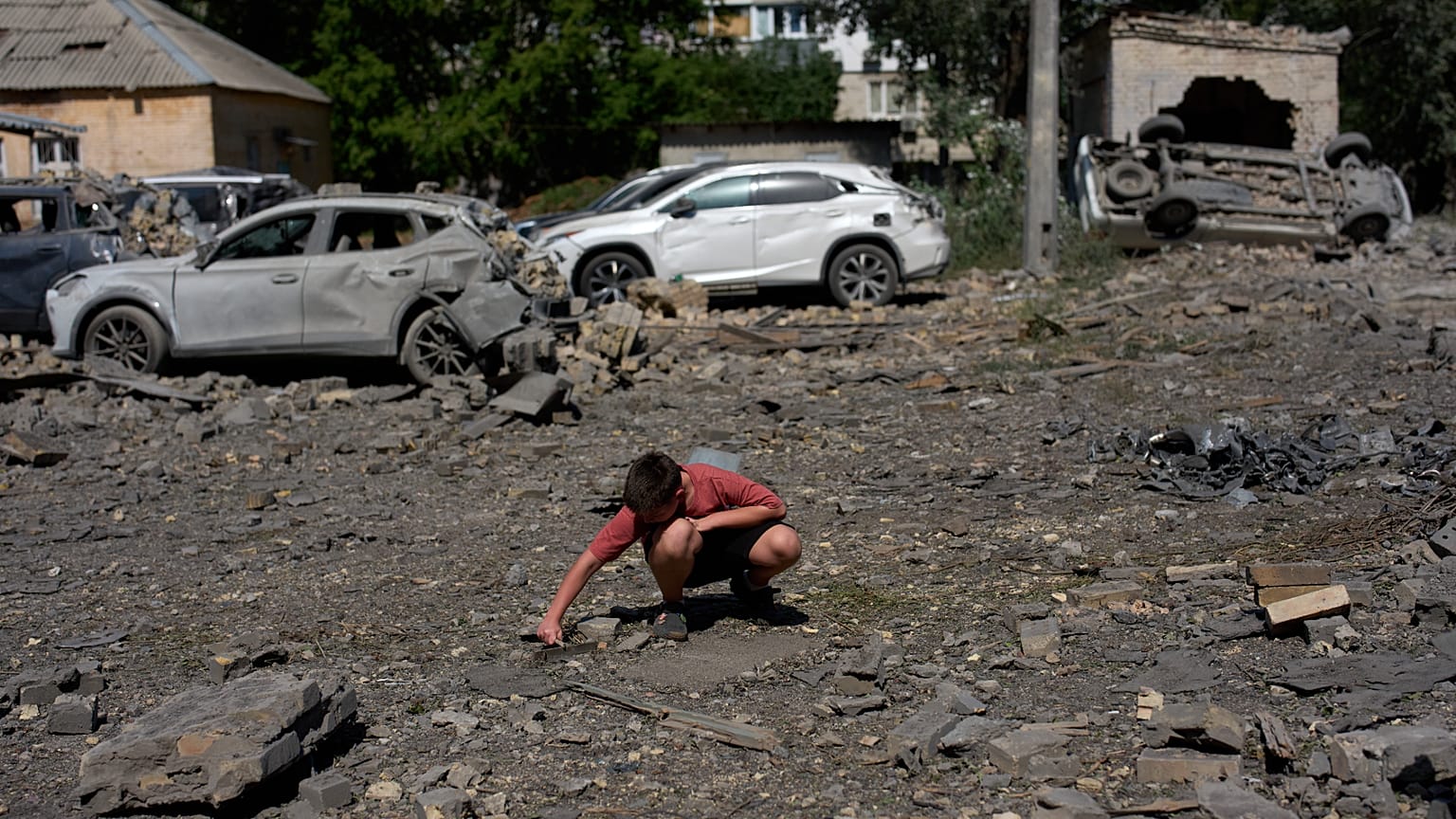 Un jeune déblaye des débris près de voitures détruites lors d’une attaque nocturne de missiles et de drones russes sur Kiev