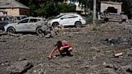 A youth removes scattered debris next to cars destroyed by an overnight Russian missile and drone attack on Kyiv
