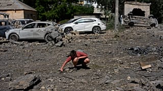Un jeune déblaye des débris près de voitures détruites lors d’une attaque nocturne de missiles et de drones russes sur Kiev