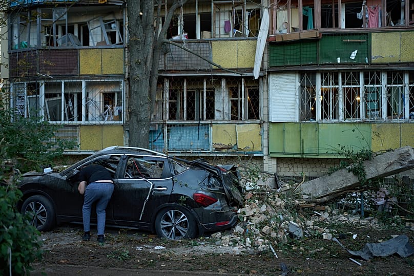 Un vecino mira dentro de un coche destruido junto a edificios residenciales gravemente dañados tras un ataque nocturno ruso en Kiev, el 20 de agosto de 2026