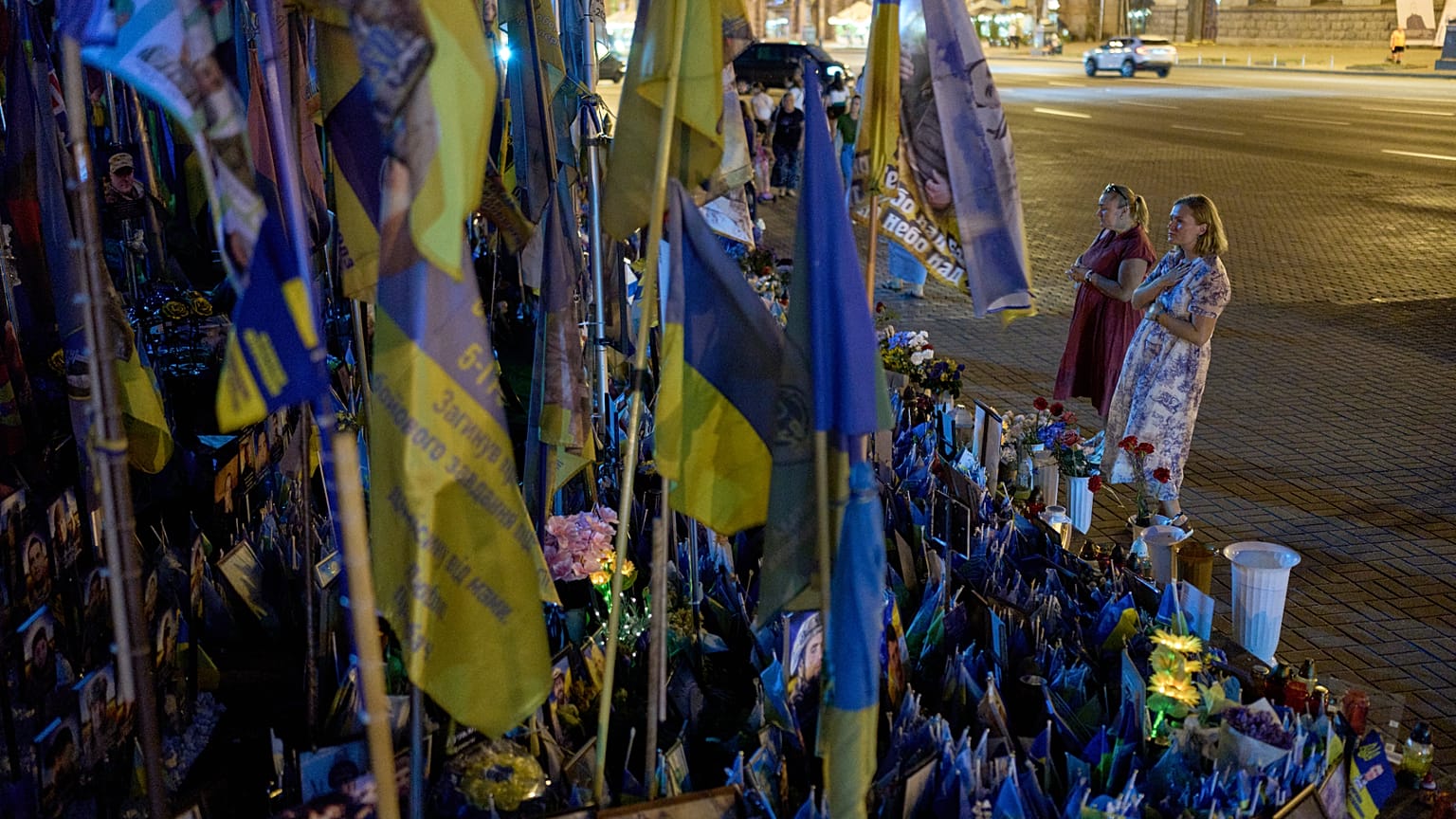 Women pray before a memorial of Ukrainian flags and photographs displayed in memory of civilians and soldiers killed during the war with Russia in central Kyiv, Friday.