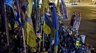Women pray before a memorial of Ukrainian flags and photographs displayed in memory of civilians and soldiers killed during the war with Russia in central Kyiv, Friday.