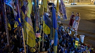 Women pray before a memorial of Ukrainian flags and photographs displayed in memory of civilians and soldiers killed during the war with Russia in central Kyiv, Friday.
