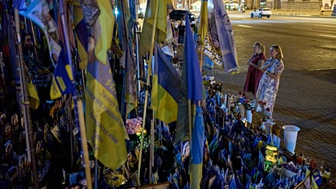 Mulheres rezam diante de um memorial com bandeiras ucranianas e fotografias em homenagem a civis e soldados mortos na guerra com a Rússia, no centro de Kiev, na sexta-feira