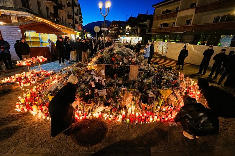 People light candles and place floral tributes outside the sealed off Le Constellation bar in Crans-Montana, 3 January, 2026