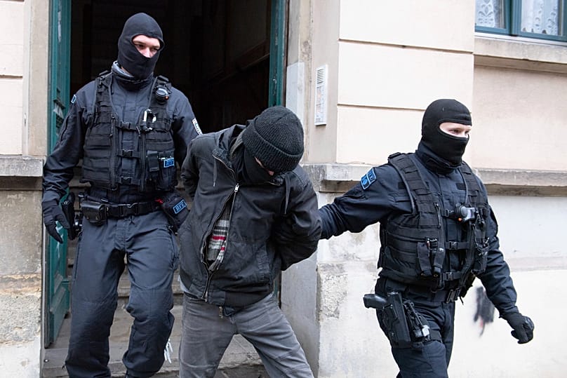 Police officers lead a suspect out of a building entrance during a raid in the Pieschen district in Dresden, 15 December, 2021