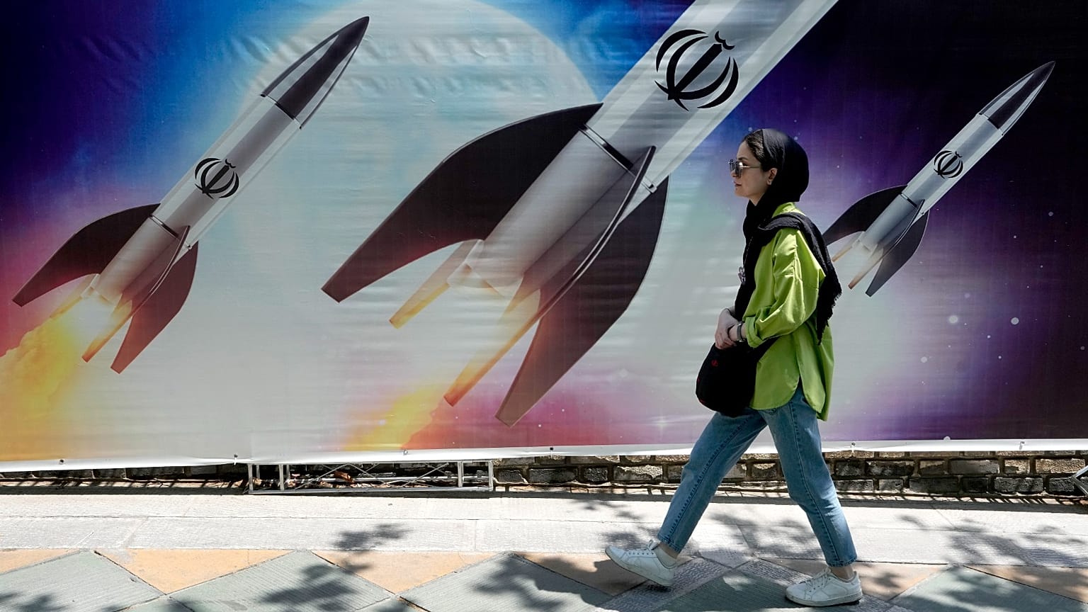  امرأة تمر أمام لافتة تظهر إطلاق صواريخ في شمال طهران، إيران، 19 أبريل 2024.