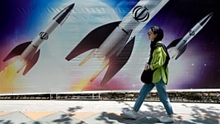  امرأة تمر أمام لافتة تظهر إطلاق صواريخ في شمال طهران، إيران، 19 أبريل 2024.