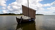 Un bateau de l'âge viking reconstruit navigue sur le Limfjord, illustrant les talents maritimes qui ont permis aux Vikings de voyager au-delà de la Scandinavie.