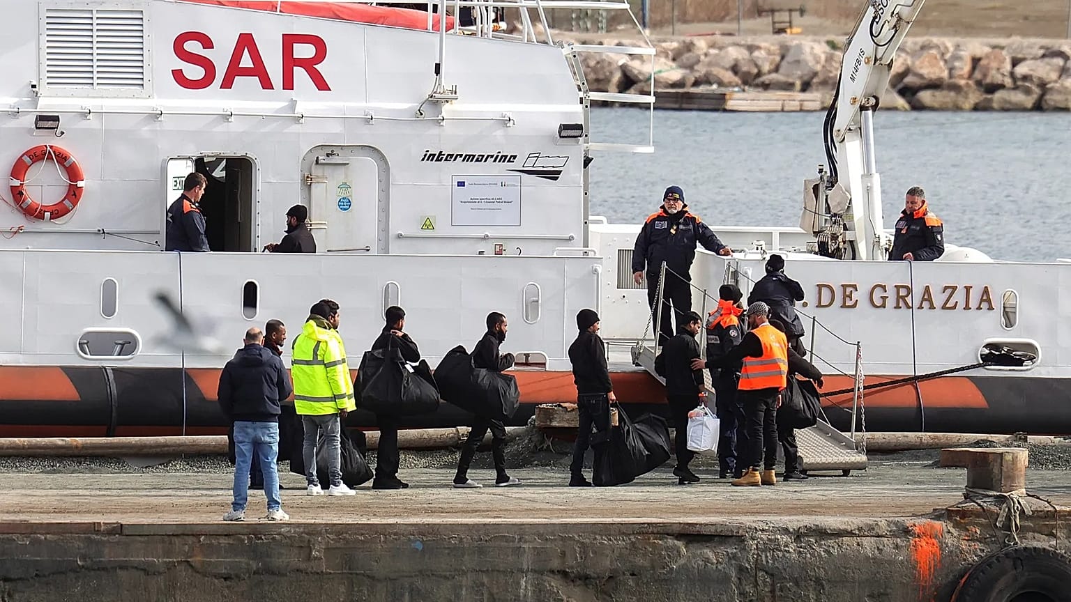 Migrants board an Italian Coast Guard vessel as part of a transfer operation from the asylum processing centres at the port of Shengjin, Albania.