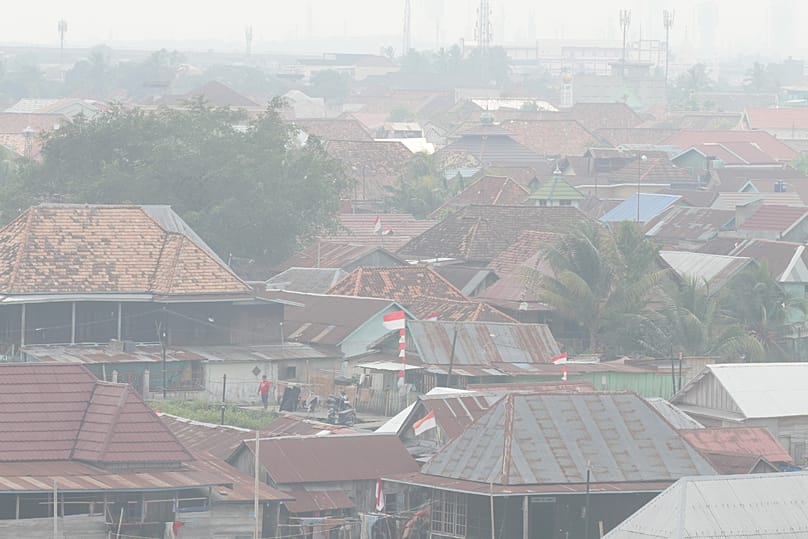 A man stands among houses as haze from wildfires blankets the city of Palembang, 25 August, 2026