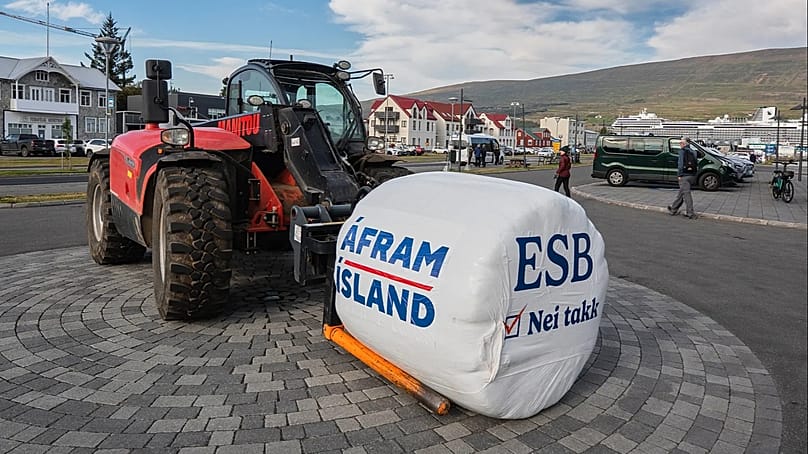 A loader carries a hay bale bearing the slogans "Afram Island" and "ESB Nei takk," which mean "Go Iceland" and "EU No Thanks" in Akureyri, Iceland, 20 August 2026. 