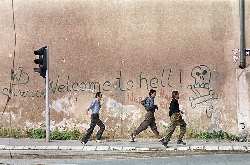 FILE: Three men run for cover past graffiti reading: "Welcome To Hell" as sniper fire rings out along Sarajevo's notorious "sniper alley" in Sarajevo, 9 June 1993
