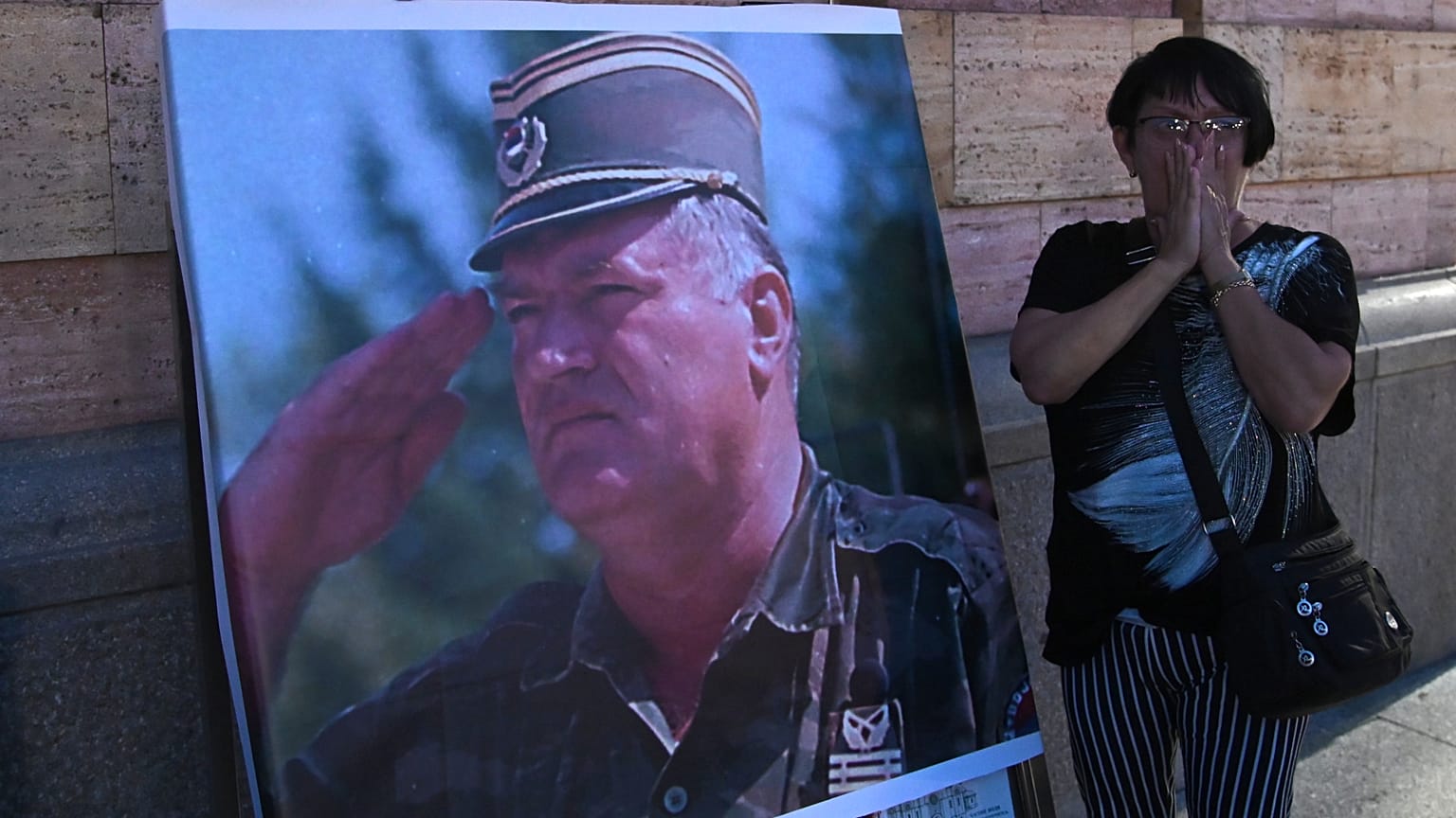 Una donna reagisce di fronte a un manifesto dell'ex generale serbo-bosniaco Ratko Mladić, all'esterno di una chiesa a Banja Luka, in Bosnia-Erzegovina, giovedì 27 agosto 2026.