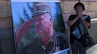 Una donna reagisce di fronte a un manifesto dell'ex generale serbo-bosniaco Ratko Mladić, all'esterno di una chiesa a Banja Luka, in Bosnia-Erzegovina, giovedì 27 agosto 2026.