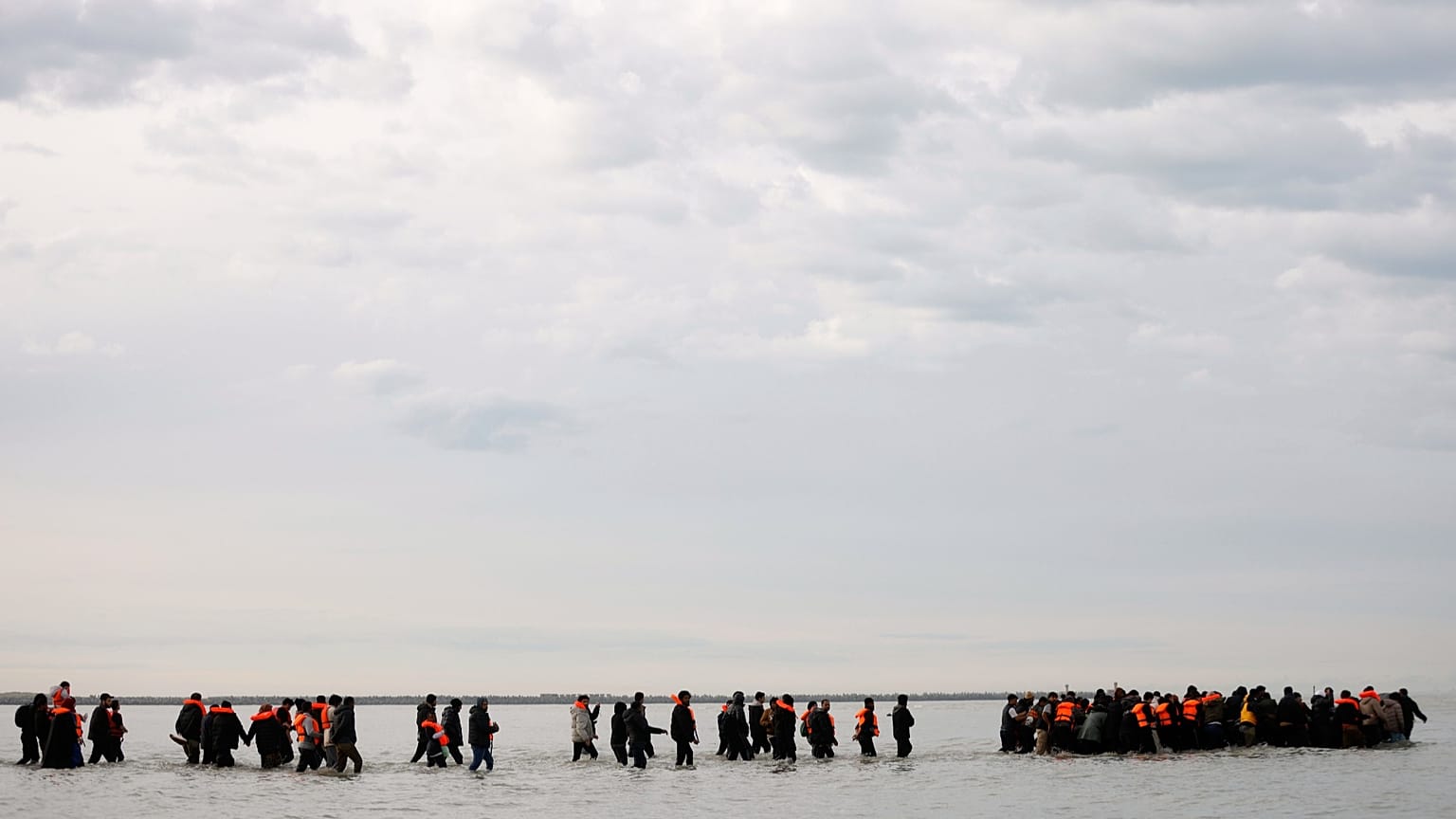 Migranti camminano in acqua per salire su una piccola imbarcazione diretta in Gran Bretagna, a Gravelines, il 6 novembre 2025.
