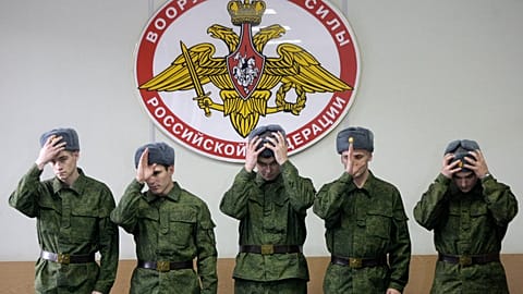 FILE: Russian military conscripts don their hats under a sign saying "The Armed Forces of the Russian Federation" at a conscription point in downtown Moscow, 26 May 2010