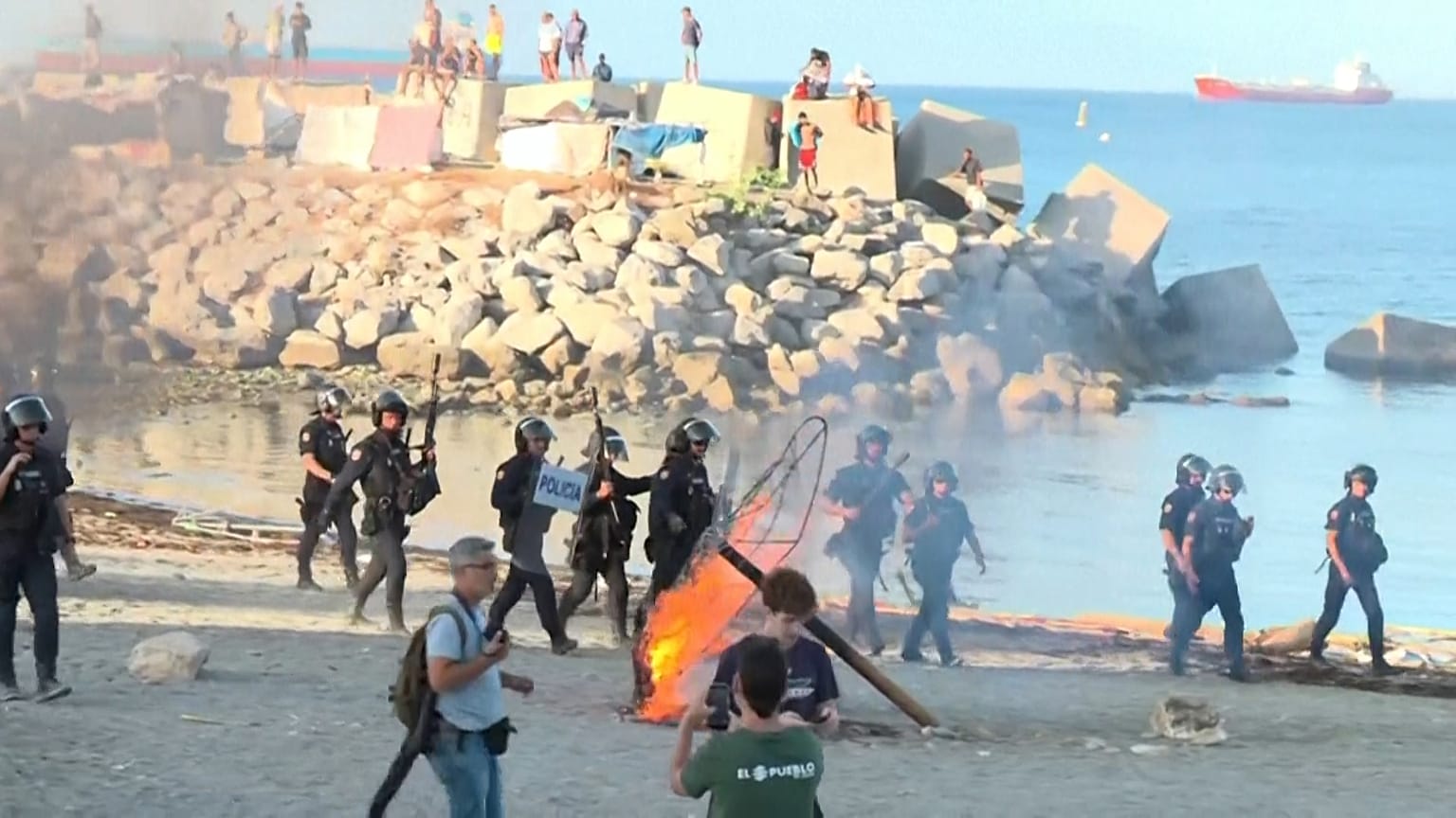 Policja zajmuje pozycje, gdy demonstranci podpalają przedmioty na plaży w Ceucie, gdzie wcześniej schronienie znaleźli migranci.