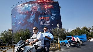 دراجات نارية تمر أمام جدارية في طهران تصور الرئيس ترامب غارقاً وسط الانفجارات، وتحمل عبارة: "انتصار عظيم! مضيق هرمز".