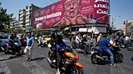 سائقو دراجات نارية يمرون بجوار لوحة إعلانية في طهران، إيران، يوم الاثنين 24 أغسطس 2026، تُظهر الرئيس الأمريكي دونالد ترامب ويدان تلتفان حول عنقه