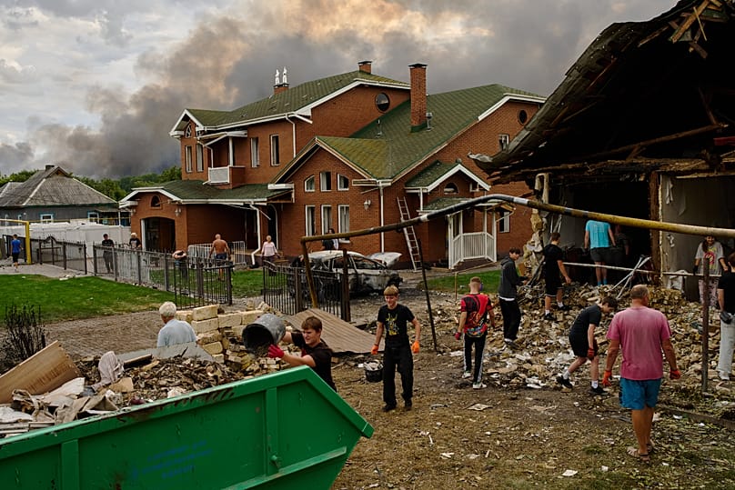 Local residents remove debris from a heavily damaged house as smoke rises from a destroyed warehouse, in the background, after Russian drone attacks  Aug. 27, 2026. 