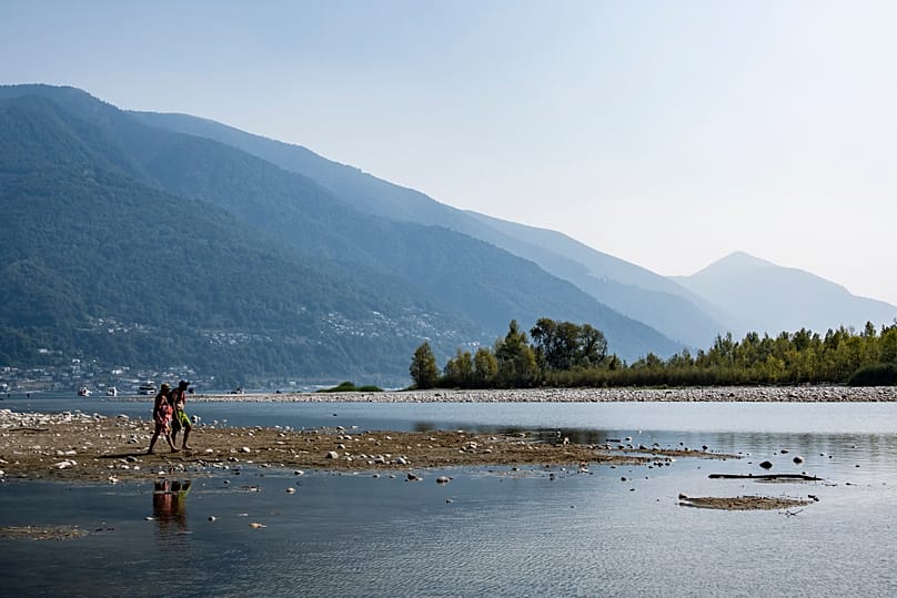 Persone camminano su una lingua di sabbia formata dal basso livello dell’acqua nel delta del fiume Maggia, dove si immette nel Lago Maggiore a Locarno, 13 agosto 2026