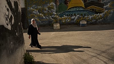 امرأة فلسطينية تسير أمام جدارية مزينة بصور تُظهر قبة الصخرة والكعبة في مخيم قلنديا للاجئين بالضفة الغربية، يوم الأربعاء 26 أغسطس 2026.