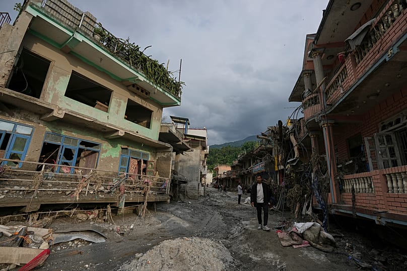 People walk along a street lined with damaged structures after flash flooding in the Devighat area of Nuwakot district in Nepal, 28 August, 2026
