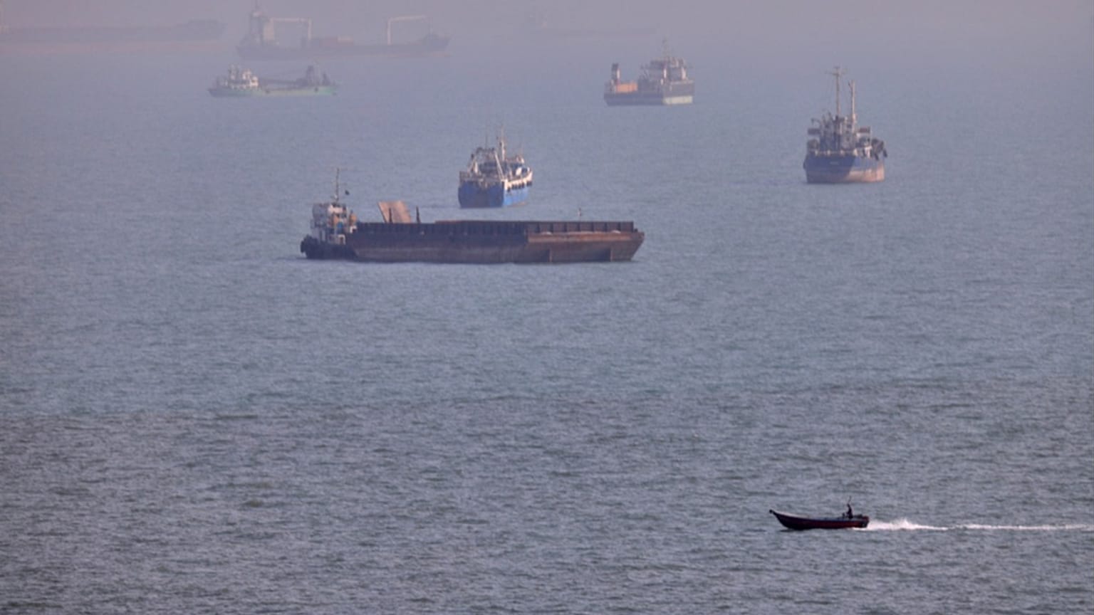 A small boat sails past cargo ships and other commercial vessels anchored in the Strait of Hormuz off Bandar Abbas, Iran, Wednesday, Aug. 5, 2026