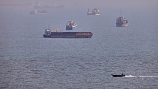 A small boat sails past cargo ships and other commercial vessels anchored in the Strait of Hormuz off Bandar Abbas, Iran, Wednesday, Aug. 5, 2026