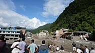 Locals watch as bulldozers and cranes work to remove debris in Trishuli