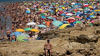 Um homem está sentado ao sol na praia de Carcavelos, nos arredores de Lisboa, na sexta-feira, 8 de julho de 2022