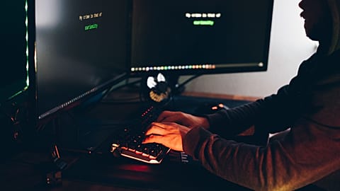 Silhouette of a person typing on a computer in a dimly lit room, emphasizing cybersecurity threats.