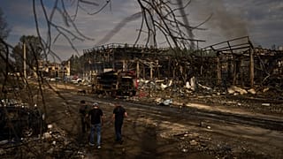 People walk past destroyed vehicles and debris scattered the day after a Russian attack struck a warehouse in Myla, 30 August, 2026