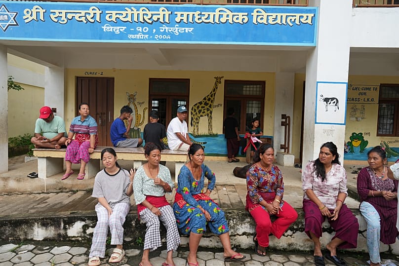 Flood survivors sit outside a school that has been turned into a temporary shelter following the floods in Bidur, 1 September, 2026