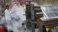 Steam comes out of a machine near a worker at a textile factory on a hot day in Sachin near Surat, India.