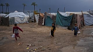 أطفال فلسطينيون نازحون يسيرون عبر مخيم خيام غارق بالمياه عقب هطول أمطار غزيرة في دير البلح، وسط قطاع غزة، الثلاثاء 24 فبراير/شباط 2026. (صورة من وكالة أسوشيتد برس/عبد الكريم ح