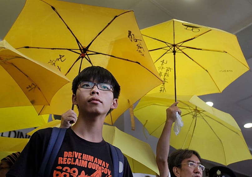 FILE - Hong Kong teenage student leader Joshua Wong, left, stands in front of yellow umbrellas outside a magistrates' court in Hong Kong, on 2 September, 2015