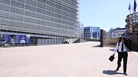 Brüksel'in AB bölgesinde yürüyen bir adam, güneşten korunmak için takım elbise ceketini kullanıyor, 25 Haziran 2026