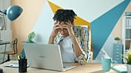 A young man looks frustrated while working on his laptop in a modern home office.