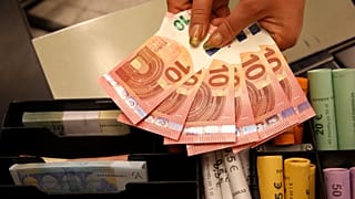A Thursday, Jan. 1, 2015 photo from files showing euro coins and banknotes shown by a salesclerk at a shop in Vilnius, Lithuania