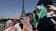 FILE - Stephanie Touissaint, foreground, uses a fan to keep cool in the sweltering heat at Eiffel Tower Stadium during a beach volleyball match at the 2024 Summer Olympics, 