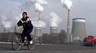 FILE - A boy cycles past a cooling towers of a coal-fired power plant in Dadong, Shanxi province, China, 3 Dec. 2009.