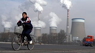 FILE - A boy cycles past a cooling towers of a coal-fired power plant in Dadong, Shanxi province, China, 3 Dec. 2009.